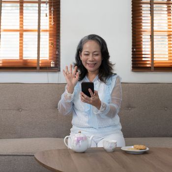 Asian old woman talking on the phone in the living room at home.