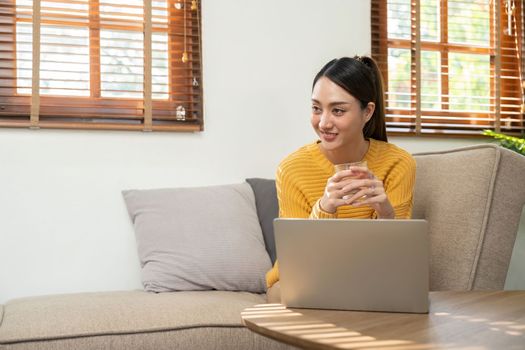 Happy Asian woman while using her laptop in the living room. work from home.