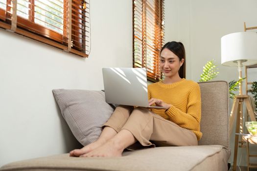 Happy Asian woman while using her laptop in the living room. work from home.