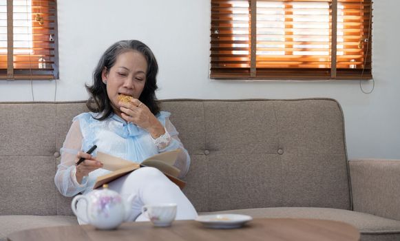 Asian elderly woman relaxing reading a book in the living room at home.