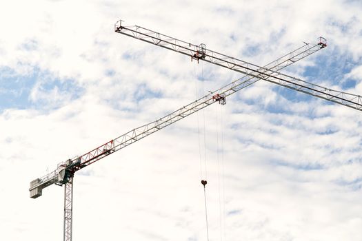 Two tower cranes with crossed booms at a construction site against a blue sky with white clouds. High quality photo