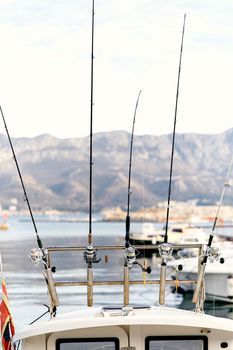 Fishing rods attached to the stern of a white yacht against the backdrop of a pier, boats, sea and mountains. Close-up. High quality photo