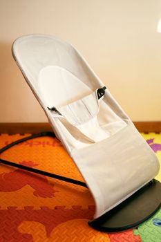 Children's white folding highchair stands on a colored rug in the room. Close-up. High quality photo