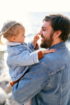 Smiling dad is holding a little girl in his arms, who touches his nose with a finger. Close-up. High quality photo