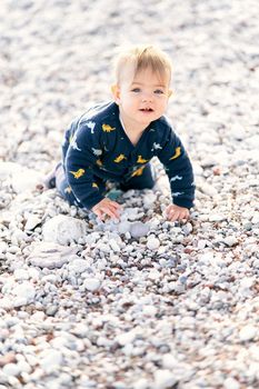 Cute little baby in overalls crawls on a pebble beach. High quality photo