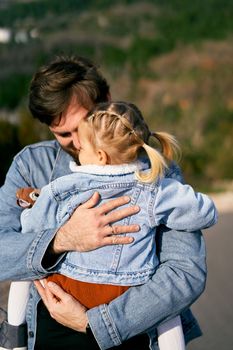 Smiling dad is holding a little girl in his arms, hugging her to his chest. Close-up. High quality photo