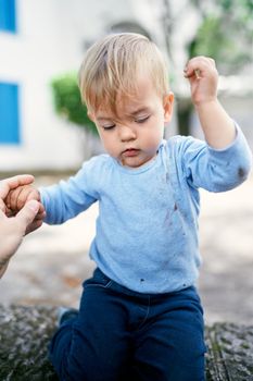 Kid sits on a stone fence in the yard with his hands up. High quality photo