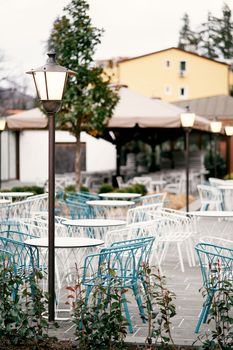 Open-air restaurant. Wicker chairs and tables stand outside near glowing lanterns against the backdrop of houses. High quality photo
