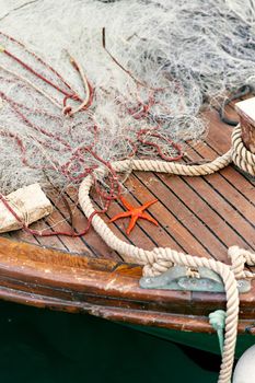 Orange starfish lies on a wooden deck of a boat near a rope and a fishing net. Close up. High quality photo