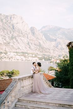 Groom hugs bride near the balustrade on the background of the mountains. High quality photo