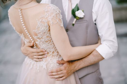 Hands of groom on the waist of bride in an embroidered lace dress. Close-up. High quality photo