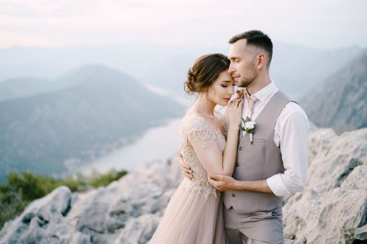 Groom hugs bride on the mountain on the background of Kotor Bay. High quality photo