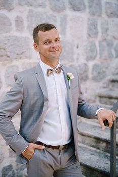 Groom stands on a stone staircase with his hand on the handrail. High quality photo