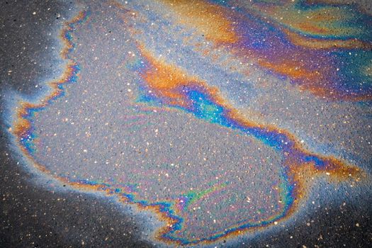 Colored texture of oil products on the asphalt in the rain. Oil dripped from the car engine onto the road