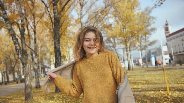 A red-haired, curly-haired girl twirls in the street in the fall