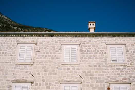Gray stone building facade with white shutters on the windows. High quality photo