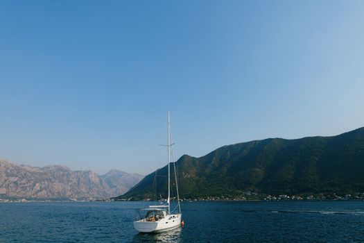 White sailing yacht stands off the coast of Perast against the backdrop of the bay. High quality photo