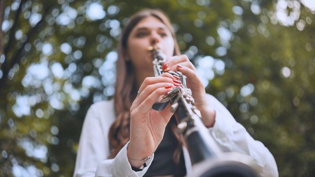 A girl plays the clarinet in the park in the summer