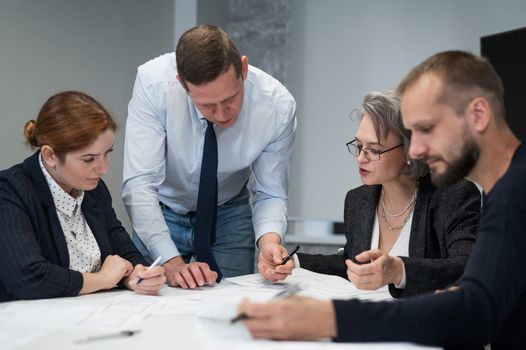 Four colleagues are discussing blueprints in a conference room in an office. Brainstorming of engineers and architects