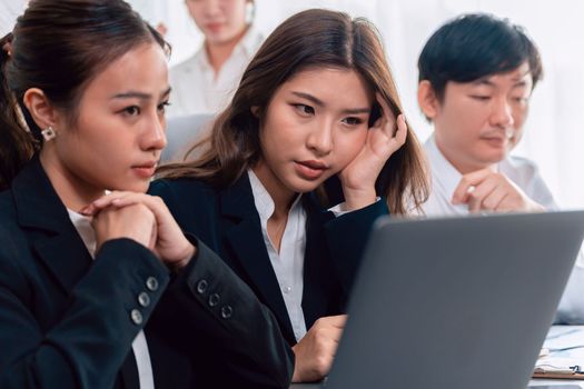 Focused businesspeople using laptop working on data analysis with serious facial expression in corporate environment at harmony office. Struggle in financial strategy planning at meeting desk.