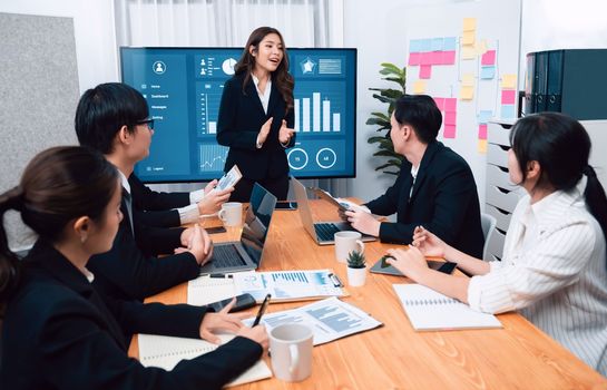 Confidence and young asian businesswoman give presentation on financial business strategy in dashboard report display on screen to colleagues in conference room meeting as harmony in workplace concept