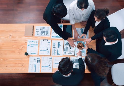 Top view hand holding gear by businesspeople wearing suit for harmony synergy in office workplace concept. Group of people hand making chain of gears into collective form with dashboard report papers.