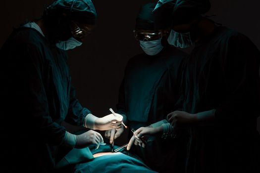 Surgical team performing surgery to patient in sterile operating room. In a surgery room lit by a lamp, a professional and confident surgical team provides medical care to an unconscious patient.