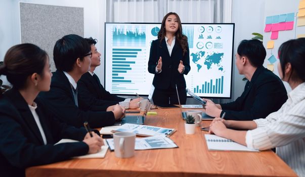 Confidence and young asian businesswoman give presentation on financial business strategy in dashboard report display on screen to colleagues in conference room meeting as harmony in workplace concept