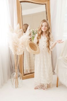 A beautiful teenage girl with long hair measures a straw hat in front of a mirror. Self-admiration of a blonde. selective focus