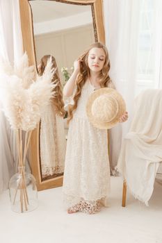 A beautiful teenage girl with long hair measures a straw hat in front of a mirror. Self-admiration of a blonde. selective focus