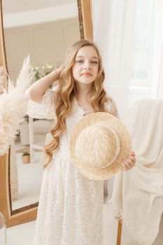 A beautiful teenage girl with long hair measures a straw hat in front of a mirror. Self-admiration of a blonde. selective focus