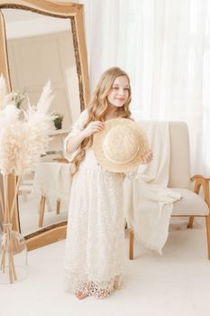 A beautiful teenage girl with long hair measures a straw hat in front of a mirror. Self-admiration of a blonde. selective focus