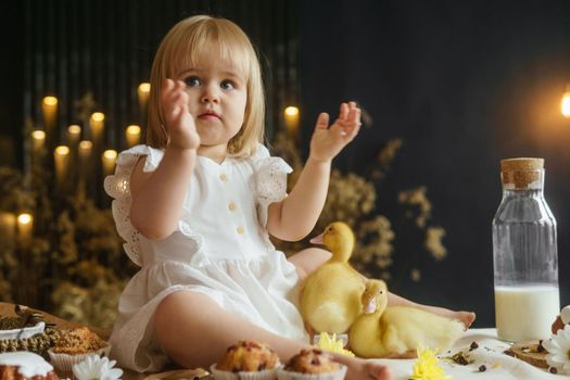 A little girl is sitting on the Easter table and playing with cute fluffy ducklings. The concept of celebrating happy Easter