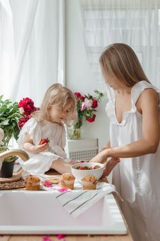 A little blonde girl with her mom on a kitchen countertop decorated with peonies. The concept of the relationship between mother and daughter. Spring atmosphere.