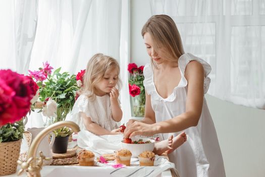 A little blonde girl with her mom on a kitchen countertop decorated with peonies. The concept of the relationship between mother and daughter. Spring atmosphere.