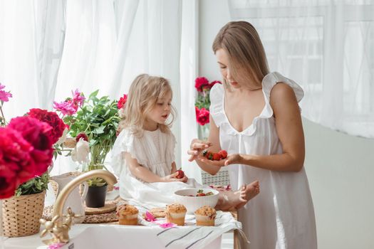 A little blonde girl with her mom on a kitchen countertop decorated with peonies. The concept of the relationship between mother and daughter. Spring atmosphere.