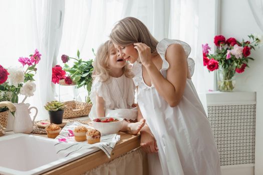 A little blonde girl with her mom on a kitchen countertop decorated with peonies. The concept of the relationship between mother and daughter. Spring atmosphere.