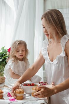 A little blonde girl with her mom on a kitchen countertop decorated with peonies. The concept of the relationship between mother and daughter. Spring atmosphere.