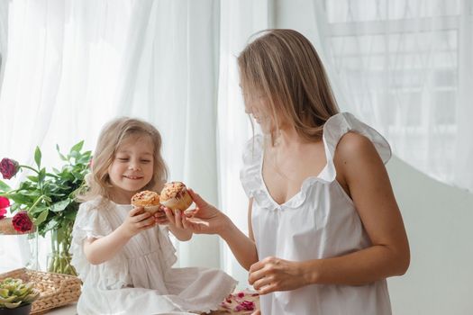 A little blonde girl with her mom on a kitchen countertop decorated with peonies. The concept of the relationship between mother and daughter. Spring atmosphere.