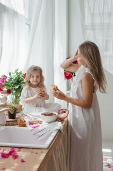 A little blonde girl with her mom on a kitchen countertop decorated with peonies. The concept of the relationship between mother and daughter. Spring atmosphere.