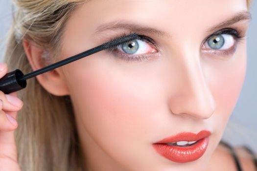 Closeup woman with blond hair putting alluring black mascara with brush in hand on long thick eyelash. Perfect fashionable cosmetic clean facial skin with beautiful eye young woman in high resolution.