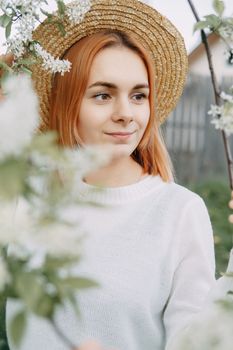 Portrait of a woman in a straw hat in a cherry blossom. Free outdoor recreation, spring blooming garden