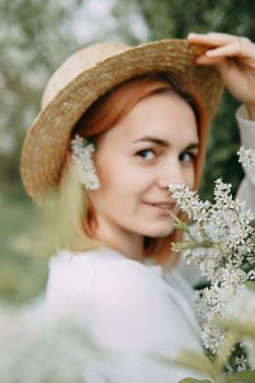 Portrait of a woman in a straw hat in a cherry blossom. Free outdoor recreation, spring blooming garden