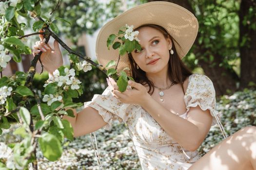 An attractive long-haired woman walks in the spring in the park of blooming apple trees. Spring portrait of a woman