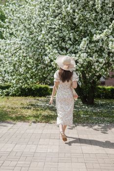 An attractive long-haired woman walks in the spring in the park of blooming apple trees. Spring portrait of a woman