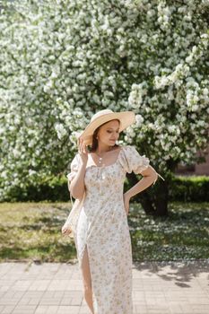 An attractive long-haired woman walks in the spring in the park of blooming apple trees. Spring portrait of a woman