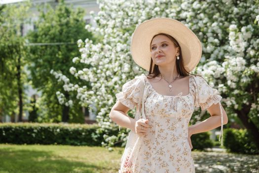 An attractive long-haired woman walks in the spring in the park of blooming apple trees. Spring portrait of a woman