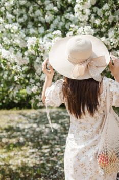 An attractive long-haired woman walks in the spring in the park of blooming apple trees. Spring portrait of a woman