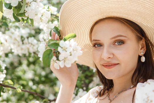 An attractive long-haired woman walks in the spring in the park of blooming apple trees. Spring portrait of a woman