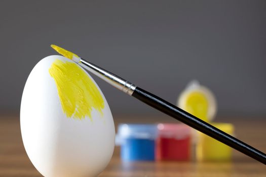 rough brush is painting a fragile easter egg with Yellow color, prepering for Holiday Happy Easter concept closeup colorful hobby